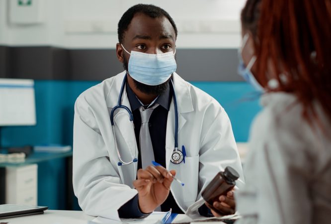 Maternity specialist and pregnant woman with face mask at checkup visit, meeting to talk about pregnancy. Future mother with baby bump asking for medical advice from physician at cabinet desk.