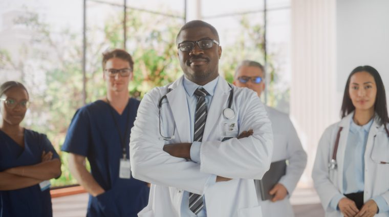 Team Portrait of a Female and Male Successful Diverse Medical Healthcare Professionals Standing as a Group in a Modern Hospital Office. African American Doctor Standing Closer to Camera